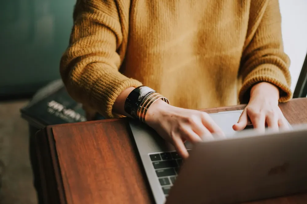 Someone typing on a laptop at a wooden desk
